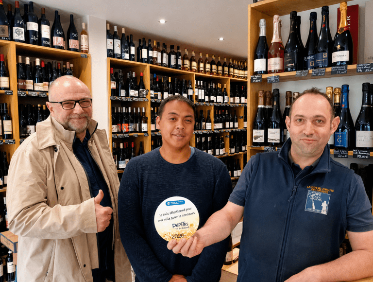 Caviste présentant sa distinction Pépites 2020 dans une cave à vins spécialisée entouré de bouteilles de vin et de champagne.