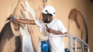 Artiste réalisant une fresque murale représentant un portrait sur un mur extérieur