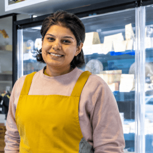 Miriam dans la fromagerie Le Bien Fait à Vitry-sur-Seine, devant les vitrines réfrigérées présentant une sélection de fromages artisanaux.