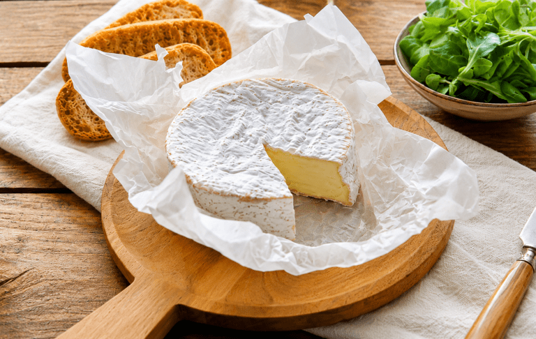 Fromage à pâte molle type brie ou camembert présenté sur une planche en bois avec du pain grillé