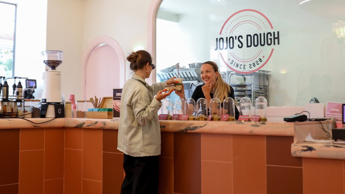 Cliente commandant des cookies artisanaux au comptoir de la boutique Jojo's Dough à Aix-en-Provence, spécialisée dans les pâtisseries gourmandes.