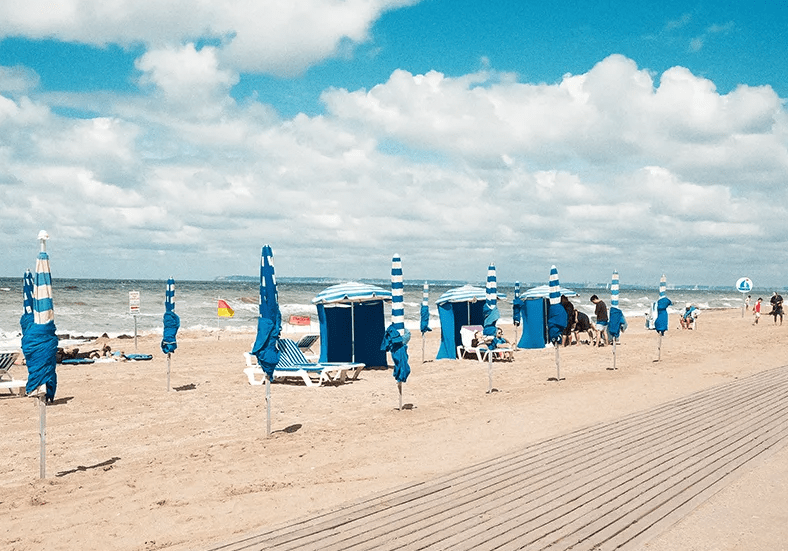 Vue de la plage de Blonville-sur-Mer avec ses cabines bleues, ses parasols, les planches en bois et le littoral normand