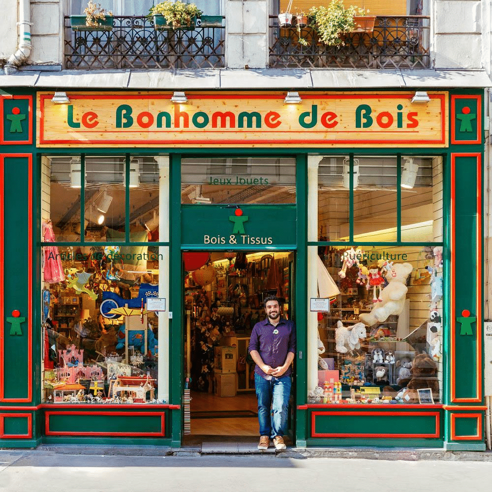 Devanture du magasin de jouets Le Bonhomme de Bois avec son commerçant à l’entrée.