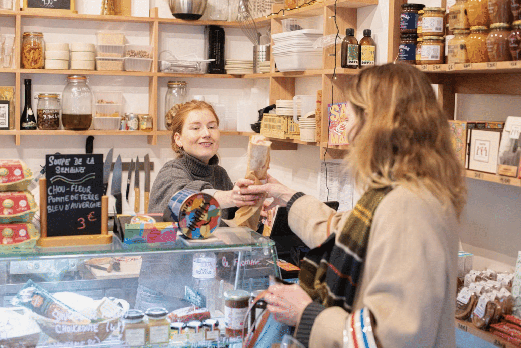 Une commerçante remet un produit à une cliente dans une boutique de proximité.