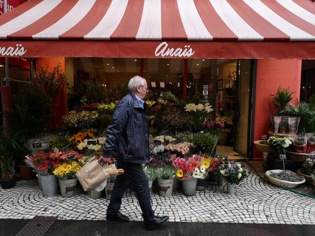 Devanture d’un fleuriste indépendant avec un étal de fleurs et un client dans une rue commerçante.