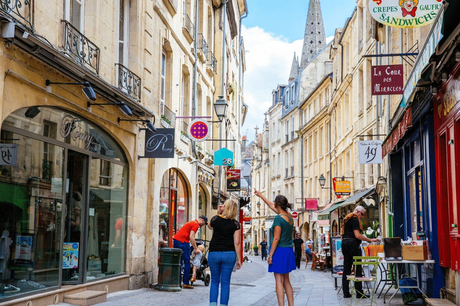 Rue commerçante de centre-ville avec des boutiques de proximité et des passants.