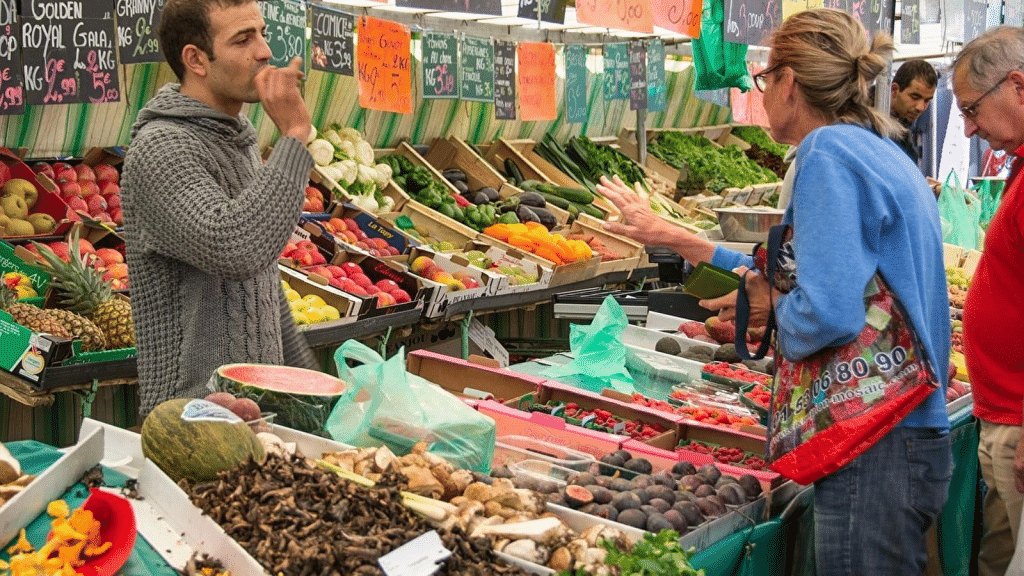 Un commerçant de marché conseille une cliente devant un étal de fruits et légumes frais.