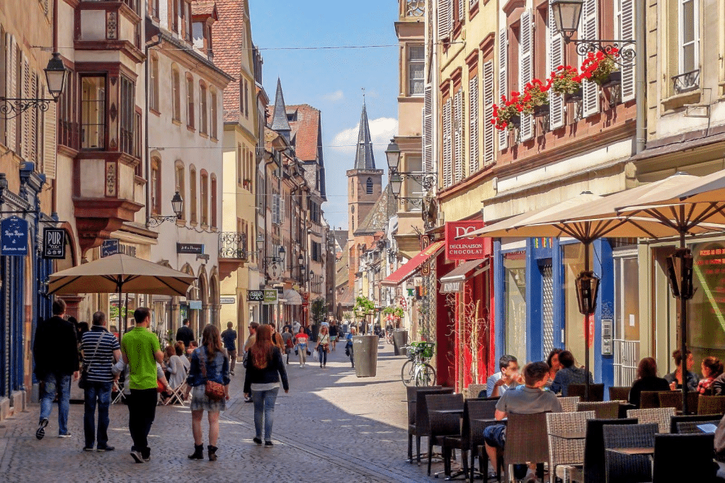 Rue commerçante animée avec boutiques, terrasses de cafés et piétons dans un centre-ville français.